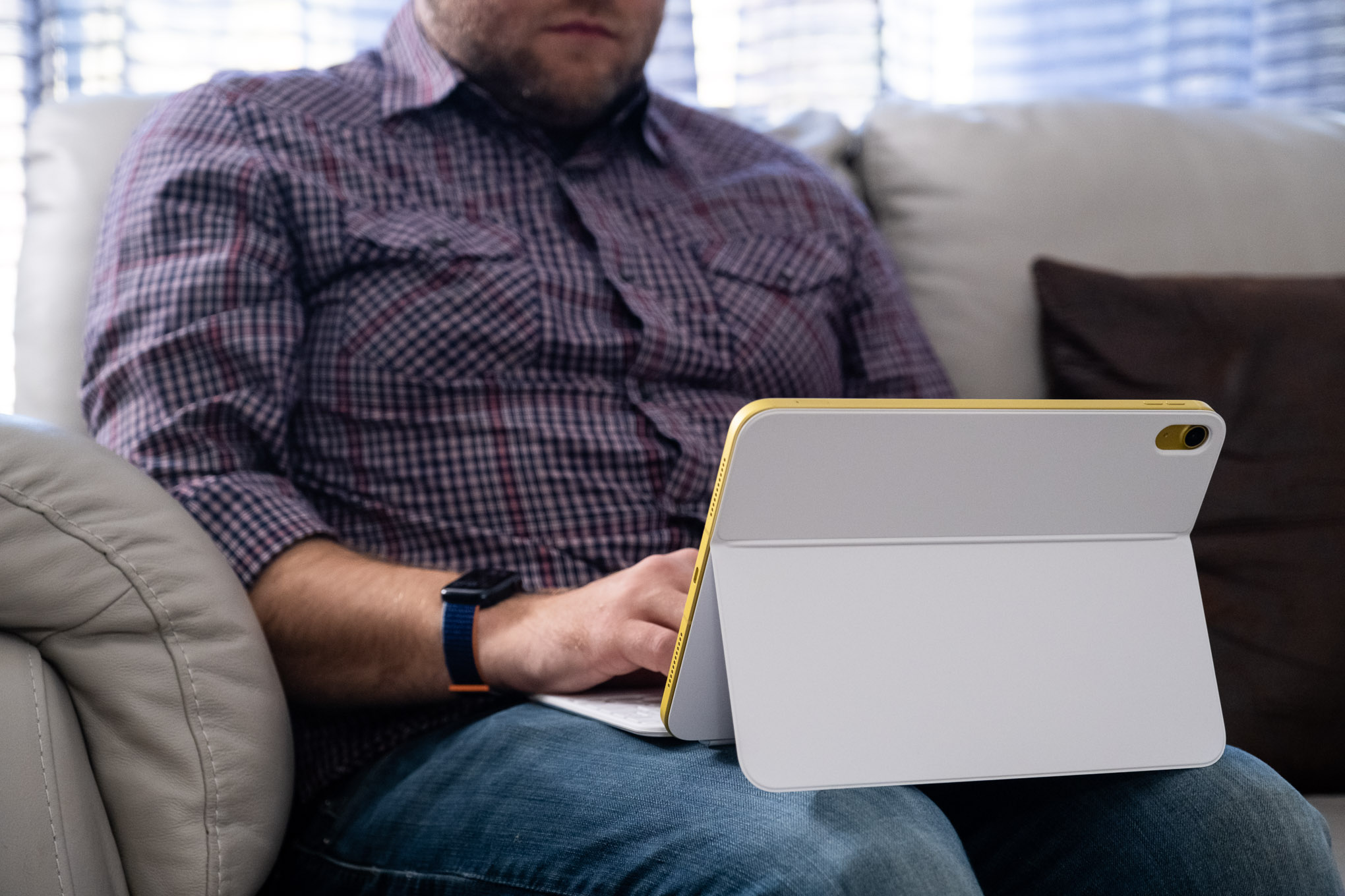 An adult man using the Apple iPad 10th gen in a Magic Keyboard folio on his lap.