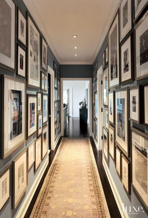 Hallway gallery with dark walls covered in many picture frames.