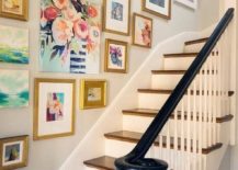 A bright stairway with a picture gallery of various sizes framed in gold frames.