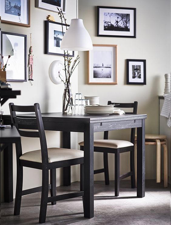 A wooden dining table is set with two chairs, while pictures adorn the walls in the background.