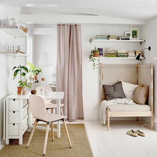 A cozy small room with white and pink colors featuring a comfortable corner chair, a table, and two chairs.