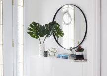 White entryway with storage and a large circular mirror.