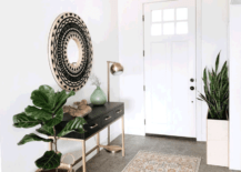 White entryway with a circular mirror, plants, and a table.