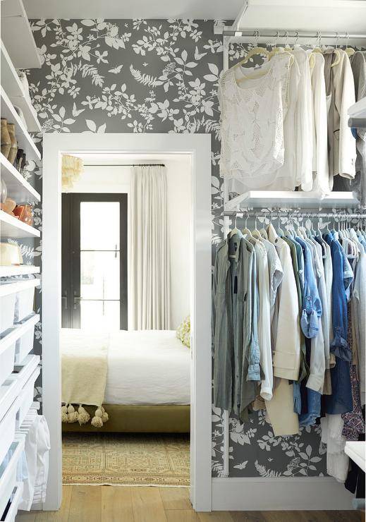 Walk-in closet designed with a charcoal gray floral wallpaper wall boasting a modular closet design with a transitional look.