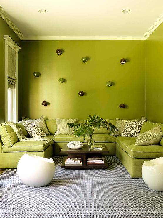 Modern avocado green living room features a brown wooden coffee table in front of a green u-shaped sectional with brown trellis pillows against a green wall.