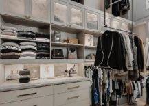 Gray walk in closet features custom drop down clothes racks, a built in dresser with brass pulls under gray shelves and a tall ceiling.