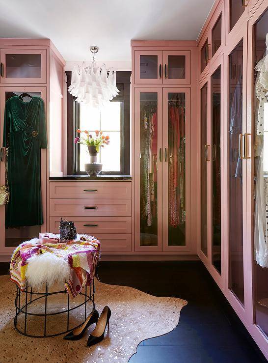Glam pink walk in closet boasts pink built-in wardrobe cabinets over a gold metallic cowhide rug atop black floor tiles and a round accent table.