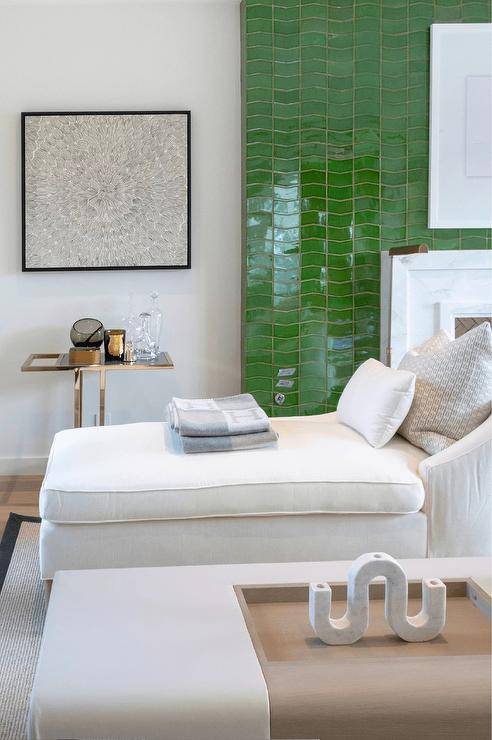 Living room features a white beveled marble fireplace on emerald green tiles, a white chaise lounge and a brass and glass accent table.