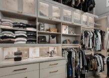 Gray walk in closet features a built in dresser under gray shelves and a tall ceiling.