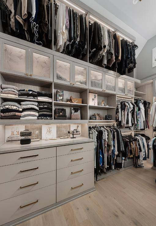 Gray walk in closet features a built in dresser under gray shelves and a tall ceiling.