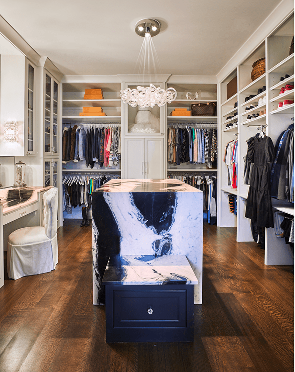 Spacious custom walk in closet features an island with a black and white marble waterfall edge and white built in shelves.