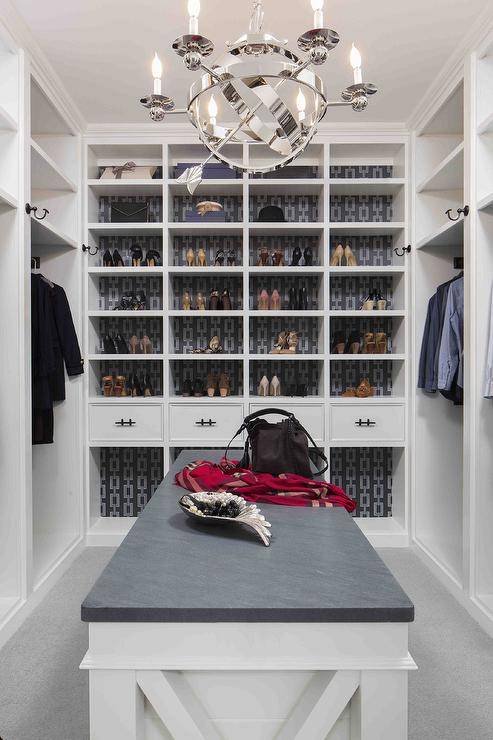 Spacious white and gray walk in closet with white and gray island features Phillip Jeffries chain link wallpaper on the back on built in shoe shelves lit by a chrome sphere lantern.