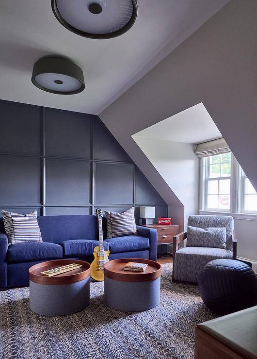 Attic family room features a blue couch on a blue paneled accent wall and round blue and brown tray coffee tables atop a blue rug and a blue accent chair.