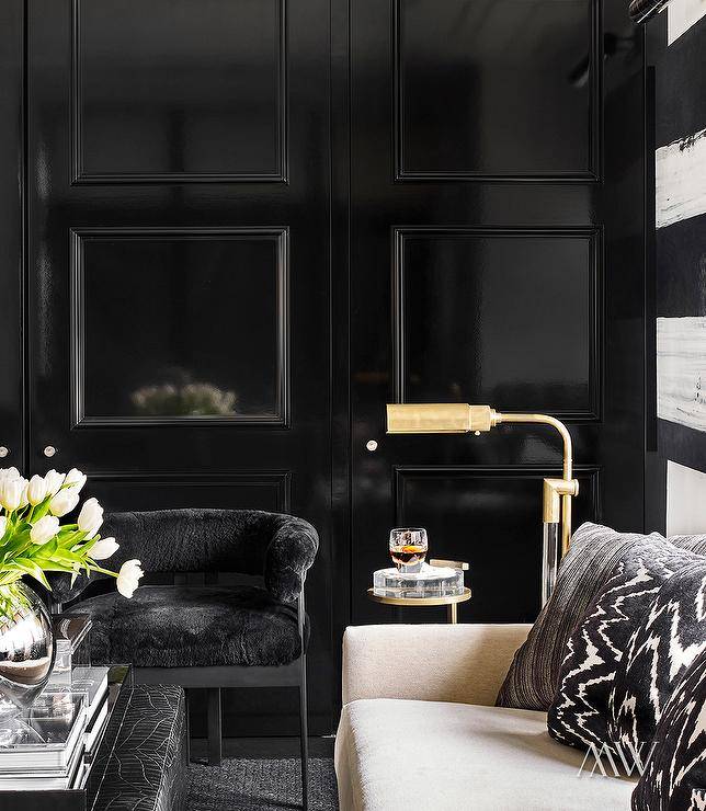 Contemporary living room features a glossy black wall trim with black velvet chair and a cream sofa with black and white pillows lit by a brass floor lamp.