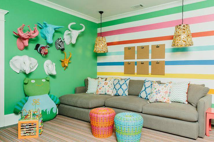 Contemporary family room features a gray sectional on a striped accent wall lit by basket lanterns, red and blue woven stools, and colorful paper mache animal heads on a green wall.