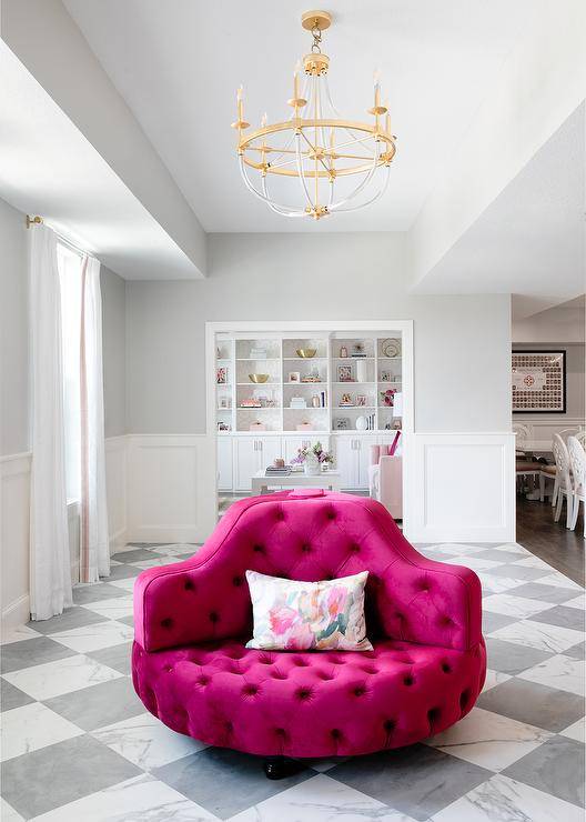 A stunning brass and glass chandelier hangs over a hot pink velvet tufted round settee placed on marble harlequin floor tiles