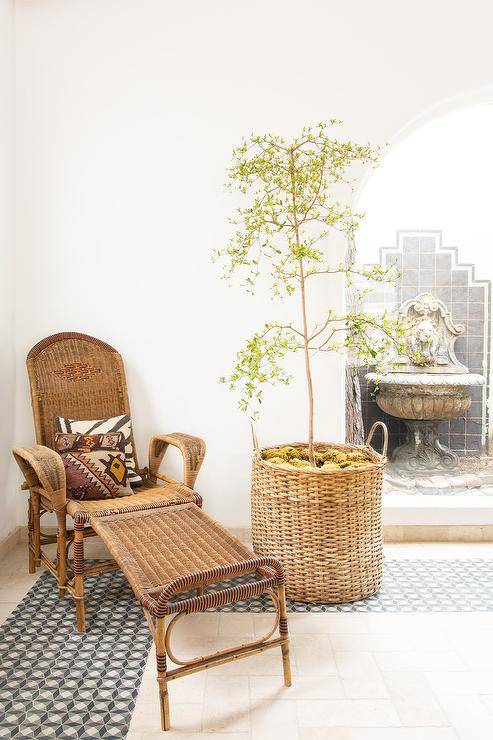 Living room features vintage wicker chair and ottoman with potted olive tree over black and white mosaic floor tiles.