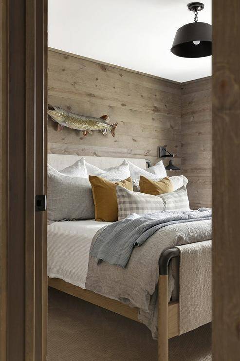 Rustic cabin bedroom features a fish mounted on plank walls over a vintage wood and metal bed accented with mustard yellow velvet pillows.