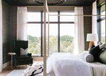 Black oak plank vaulted ceiling above a bedroom showcasing a black round chandelier with a light gray wooden canopy bed and a black bench at the foot.