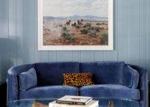 Living room features a curved blue velvet sofa with a leopard print pillow on a vertical blue plank wall with blue brown and white art, and a Noguchi coffee table