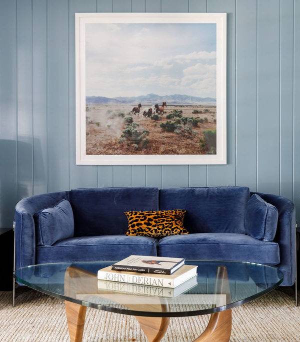 Living room features a curved blue velvet sofa with a leopard print pillow on a vertical blue plank wall with blue brown and white art, and a Noguchi coffee table