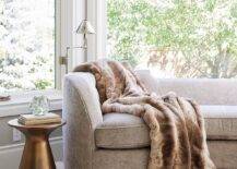 Bedroom bay window boasts a taupe brown curved sofa with a gold accent table on a white sheepskin rug.