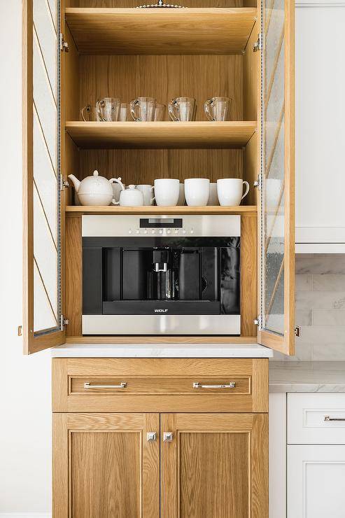 Kitchen features light brown oak coffee cabinets with seeded glass chevron pattern doors and a wolf coffee maker.