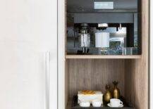 Light gray pull out coffee pod drawers are stacked beneath a shelves holding coffee mugs and a brown shelf holding a Miele coffee machine.