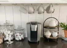 Coffee bar with glass containers, teapots, and white Keurig coffee machine.