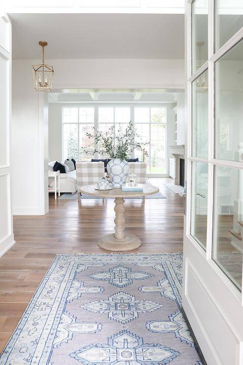 Large foyer features a blue and gray entry rug layered on white engineered oak floors, and leads to a round entryway accent table.