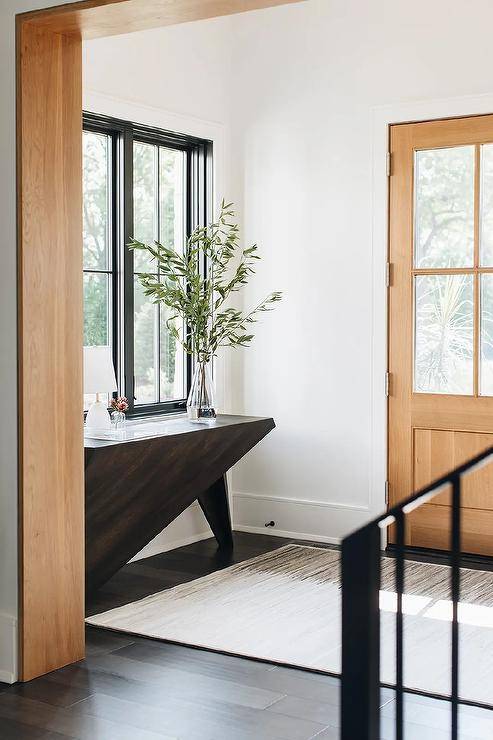 Modern entryway features a dark brown asymmetrical console table under a window and a tan rug.