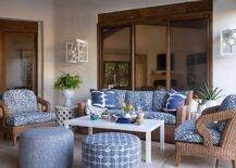 Gorgeous brown and blue covered patio features a brown wicker chairs topped with blue cushions and flanked by white accent tables. The sofa is positioned facing a white lacquer coffee table located between brown chairs. The space is finished with two blue upholstered stools.