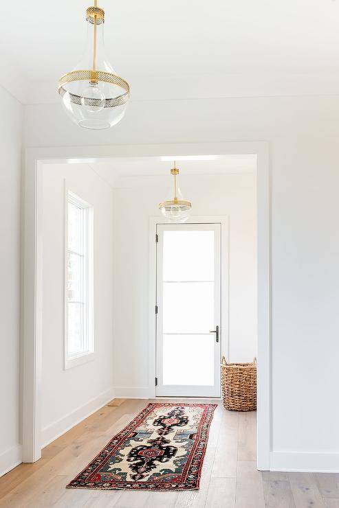 Brass and glass French lanterns in a bright and airy foyer designed with a glass front door and a red vintage runner on gray wash oak wood floors.