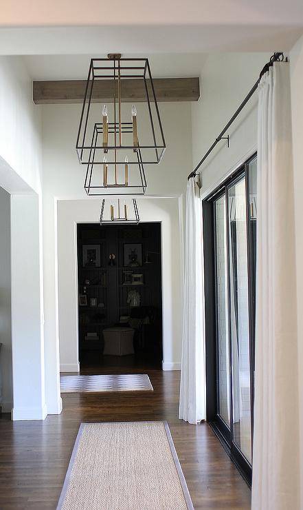 This walkway, featuring three of Circa Lighting's Morris chandeliers, features chic sliding doors that allow for the flow of natural light, custom white drapery, and a simple yet elegant seagrass rug.