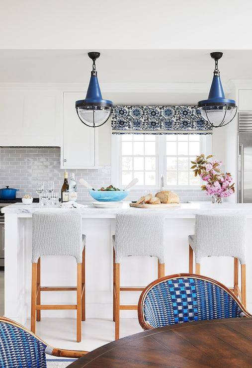 Two bold blue lanterns hang over a marble top kitchen island seating heather gray counter stools.