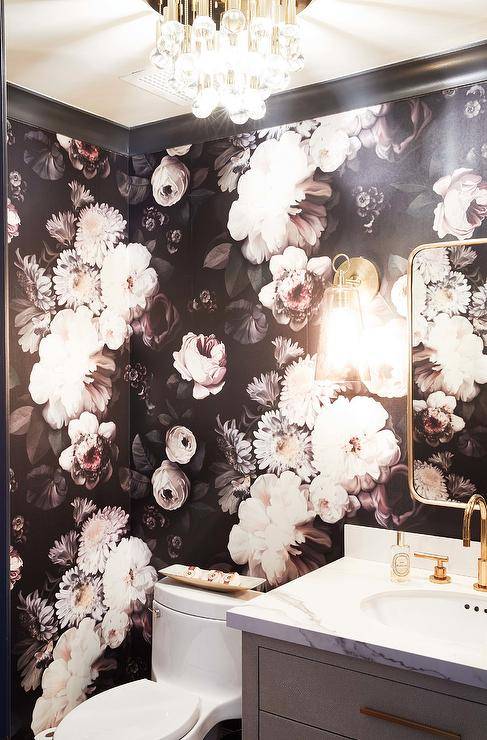 Elegant contemporary powder room is covered in Ellie Cashman Dark Floral Wallpaper and boasts a curved brass mirror hung over a gray shagreen bath vanity. The bath vanity is accented with brass hardware, a white quartz countertop and a brass gooseneck faucet.