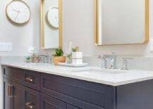Dark blue washstand with brass pulls and chrome faucets topped with a white quartz countertop. Mixed metals create complementing design from chrome faucets to brass pulls and marble floors.
