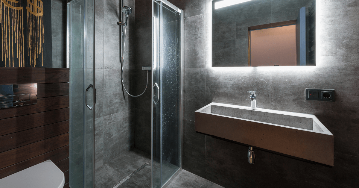 Black themed wet room bathroom with LED lighting around the vanity mirror.