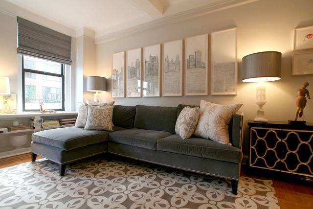 Chic city living room design with gray velvet sofa with chaise lounge, white & gray rug, vintage black & gold chest, white alabaster lamp, gray roman shade and art.