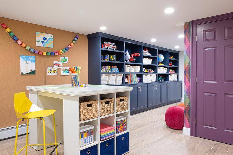 Basement craft space features a canary yellow stool placed at a high top craft table finished with cubbies and located to the side of a floor-to-ceiling cork board.