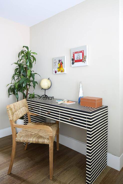 Worlds Away Sasha Desk features a black and white striped pattern with brass knobs in a boy's bedroom paired with a woven chair. A corner house plant and wall decor finish the kids work space with style.