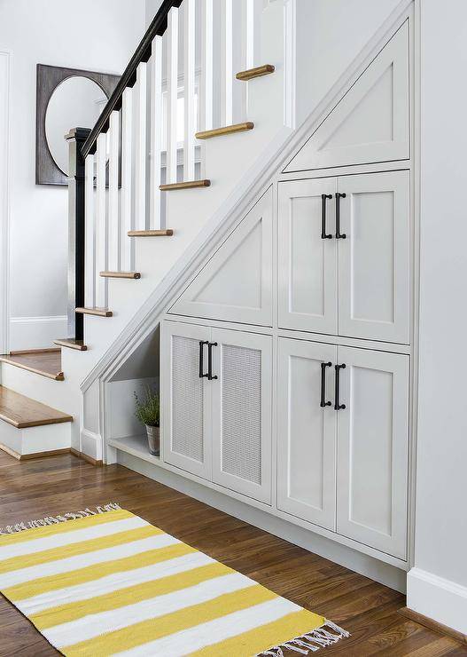 Yellow and gray foyer features under the stairs pull out cabinets alongside a yellow striped runner with fringe trim.