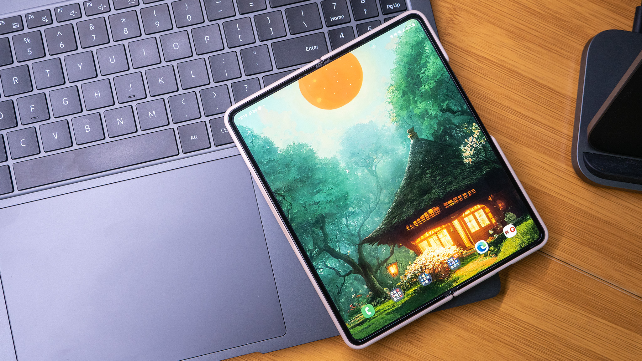 A Samsung Galaxy Z Fold 4 unfolded showing a Backdrops wallpaper on the homescreen, resting on the keyboard of a Galaxy Book 3 Ultra